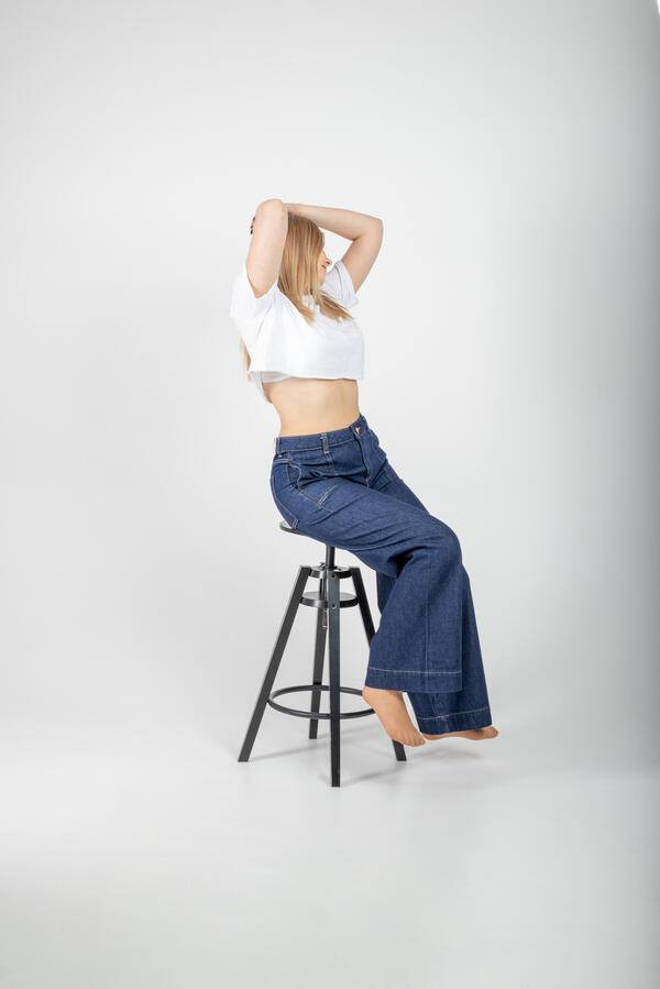 Zdjęcie portretowe wykonane w studio na którym dziewczyna ubrana w biały T-shirt oraz jeansowe spodnie pozuje na krześle