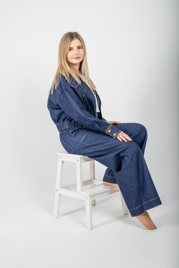 Zdjęcie portretowe wykonane w studio na którym dziewczyna ubrana w jeansową kurtkę oraz jeansowe spodnie pozuje na krześle
