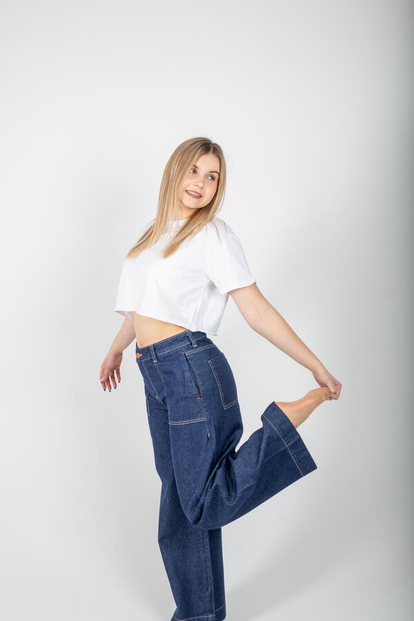 Zdjęcie portretowe wykonane w studio na którym dziewczyna ubrana w biały T-shirt oraz jeansowe spodnie pozuje na stojąco