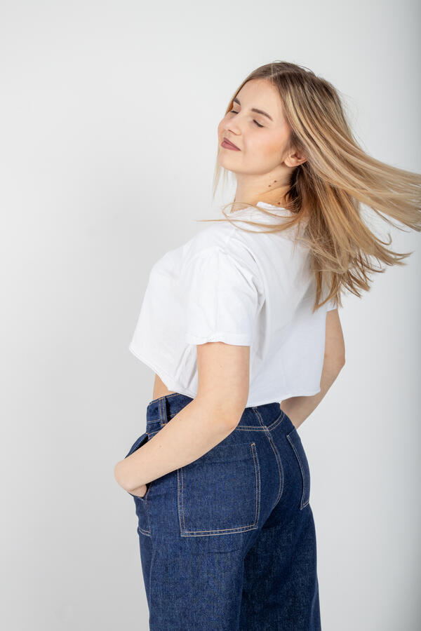 Zdjęcie portretowe wykonane w studio na którym dziewczyna ubrana w biały T-shirt oraz jeansowe spodnie pozuje na stojąco
