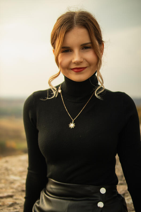 Zbliżenie uśmiechniętej kobiety w czarnym golfie na tle rozmytego krajobrazu.